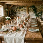 Table de mariage intime dressée pour 30 personnes dans une grange rustique avec décoration florale naturelle et chandelles en terre cuite