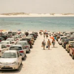 Parking bondé près de la plage de La Pelosa en Sardaigne avec des voitures alignées et la mer turquoise en arrière-plan